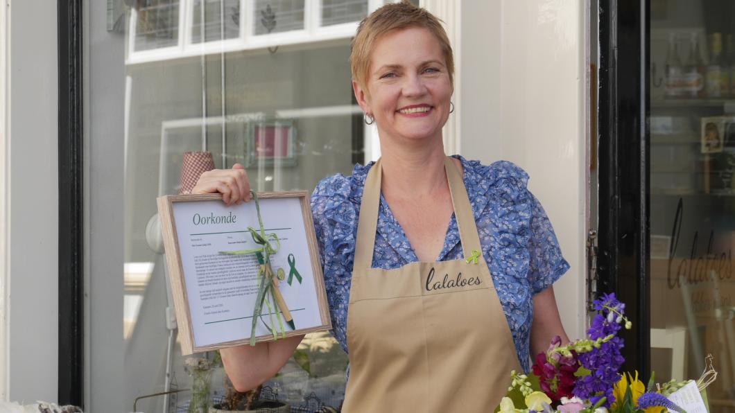 Loes van Dijk van restaurant Lalaloes, met het groen lintje opgespeld en de bijbehorende oorkonde In de hand.